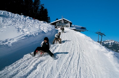Personen beim Rodeln in einer sonnigen Winterlandschaft